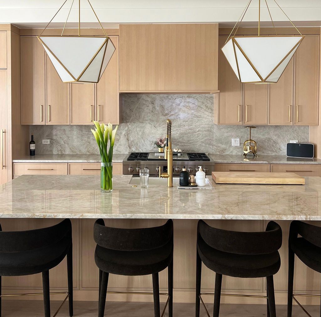 Modern kitchen with island, beige cabinets, stone backsplash, and black bar stools.