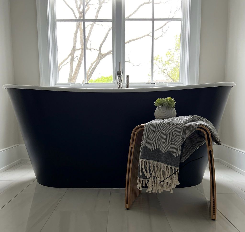 Navy blue clawfoot bathtub in front of a window, with a stool and throw blanket.