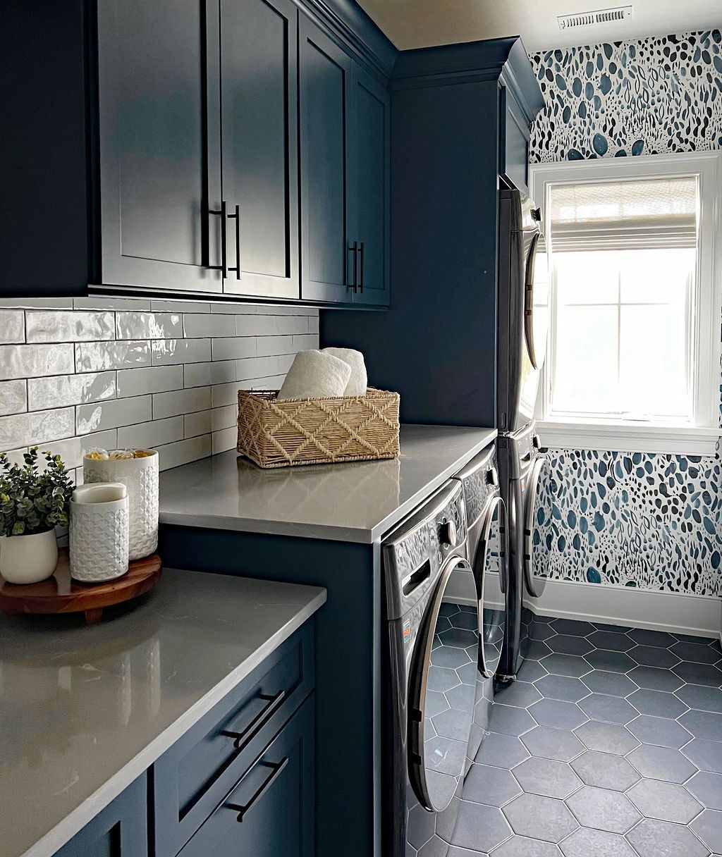 Laundry room with blue cabinets, white countertops, and patterned wallpaper.