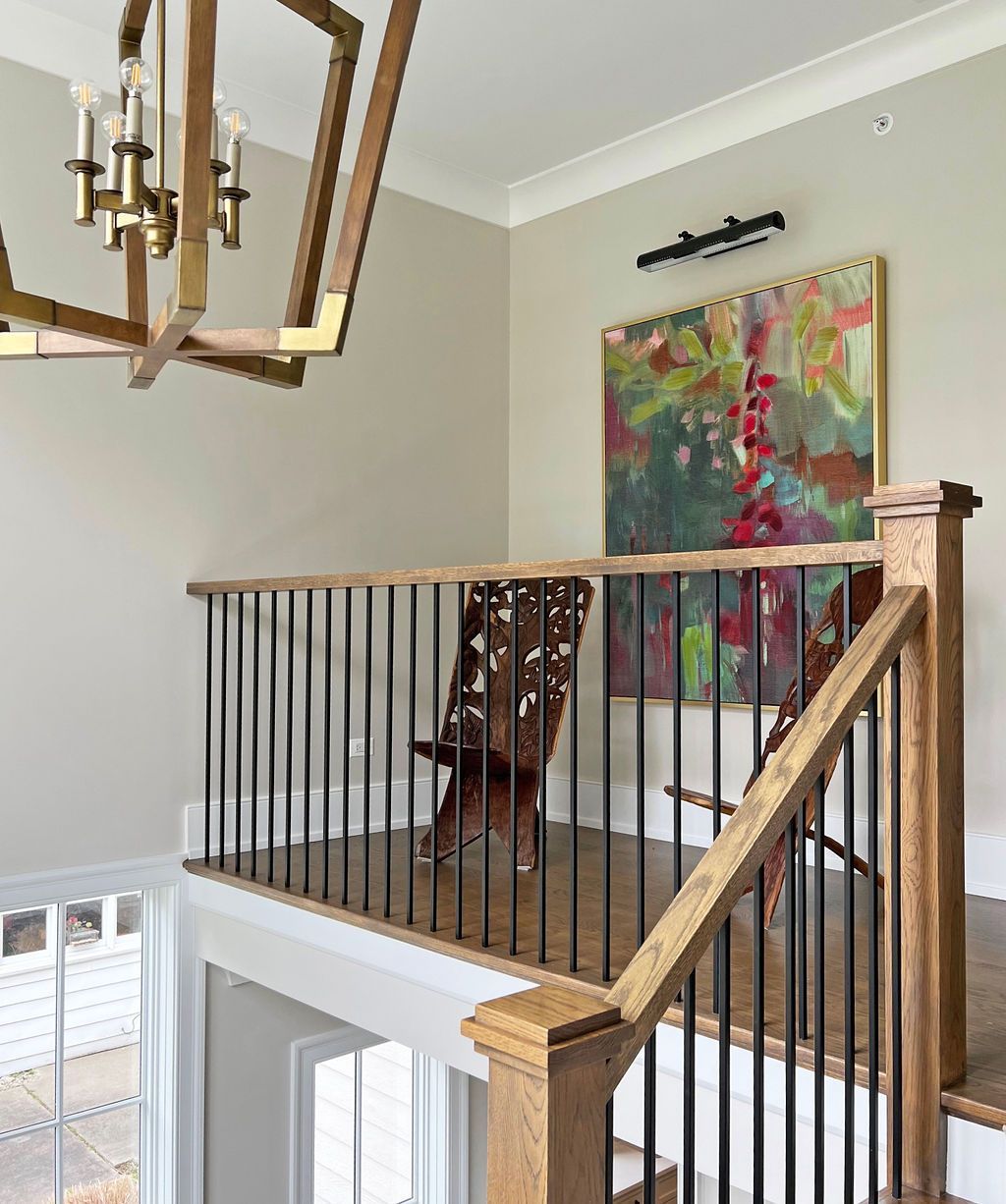 Wooden staircase landing with black railings, abstract artwork, and a geometric chandelier.