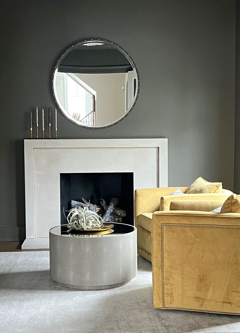 Cozy living room with gray walls, white fireplace, round mirror, yellow sofa, and a gray coffee table.