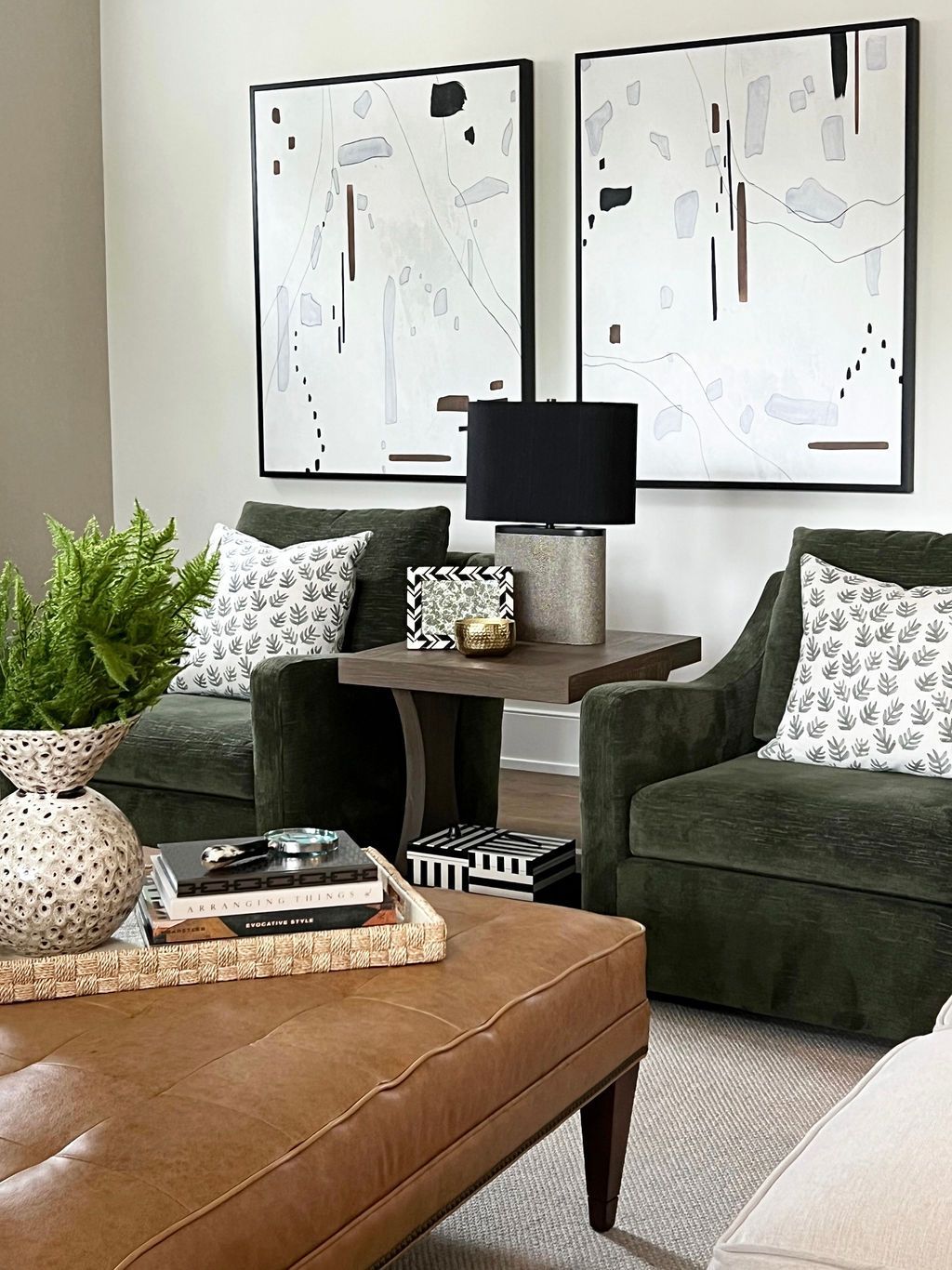 Living room with green armchairs, abstract art, and a brown leather ottoman.
