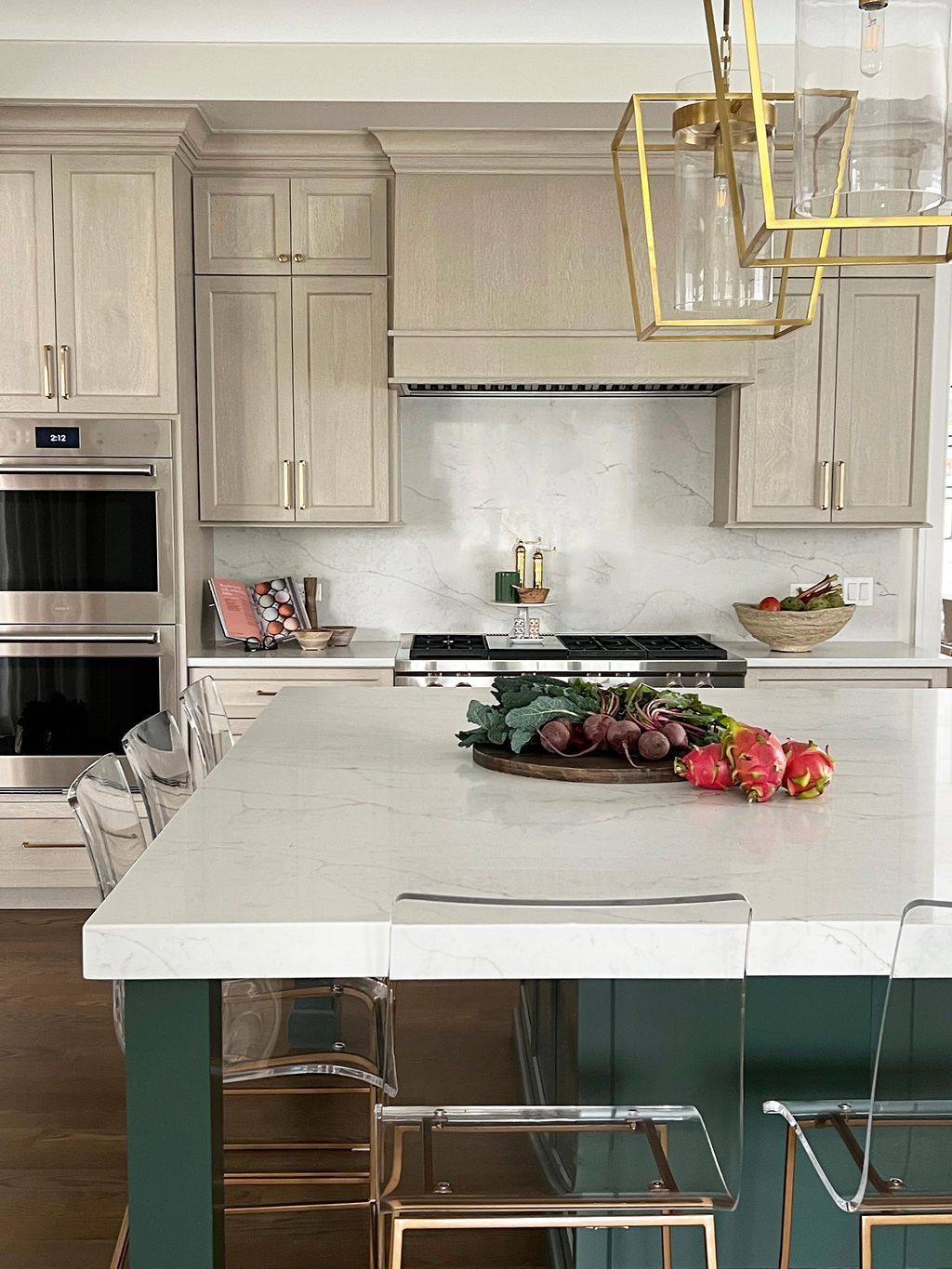Modern kitchen with green island, white countertop, vegetables, and clear bar stools.