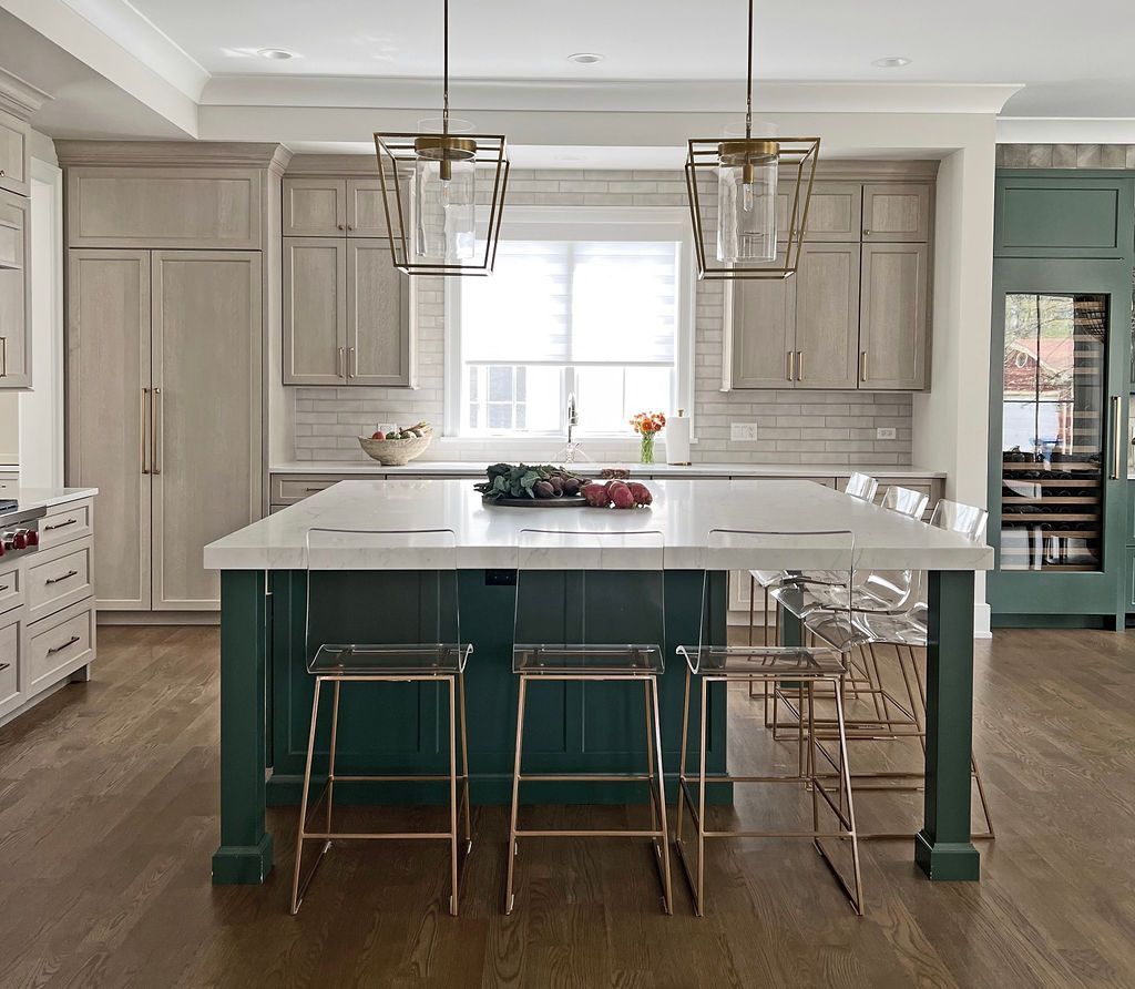 Modern kitchen with white countertops, dark green island, gold accents, and clear bar stools.