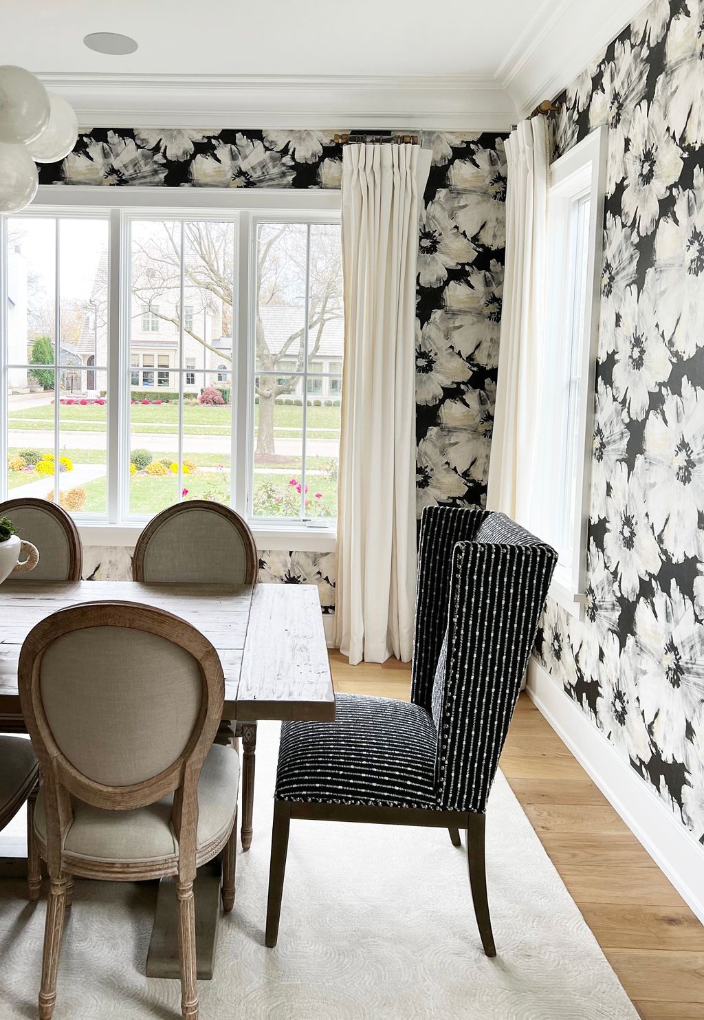 Dining room with floral wallpaper, wood table, and chairs, with a window view.
