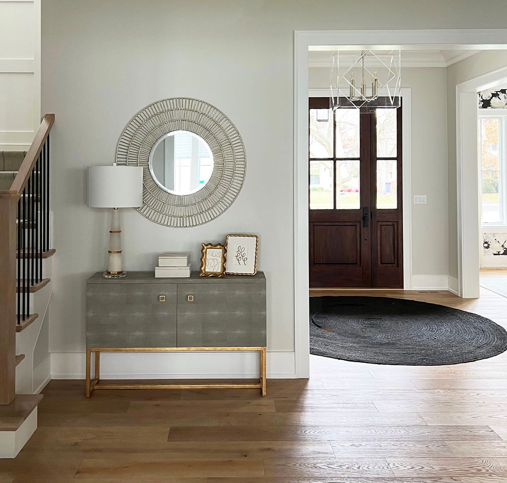 Gray entryway cabinet with lamp, mirror, and decor. Open doorway, hardwood floor.