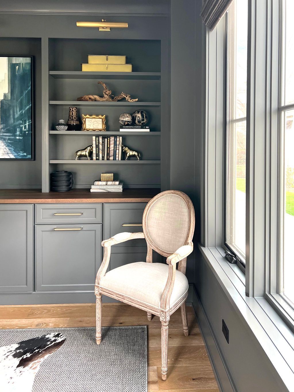 Gray home office with built-in shelves, armchair, and window; dark gray walls, light wooden floor.
