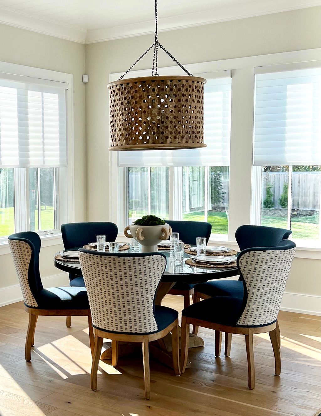 Dining room with round table, blue chairs, and woven light fixture. Windows and natural light.