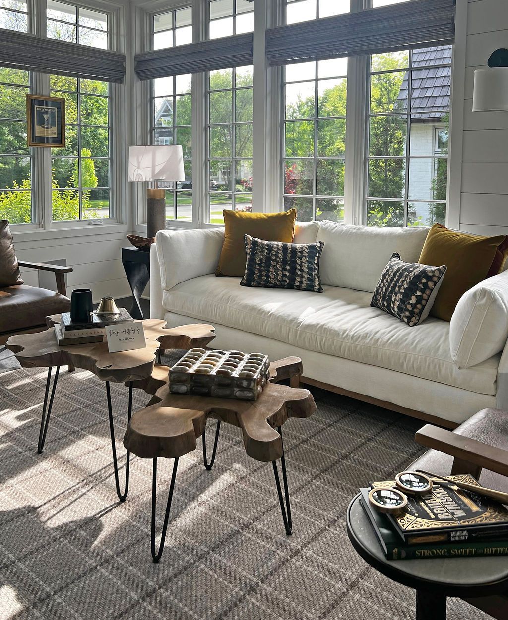Sunroom with white sofa, wood tables, and large windows with patterned shades.