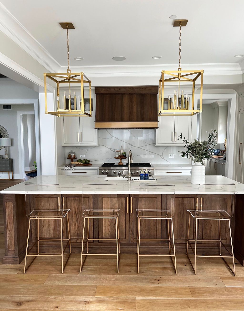 Kitchen with a wooden island, gold light fixtures, and clear bar stools.