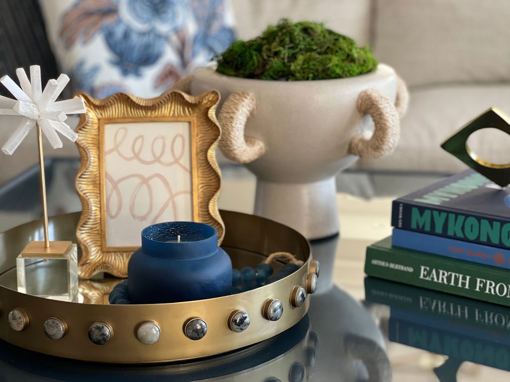 Coffee table decor: Gold tray with candle, picture frame, and sculpture. White vase with moss, and books.