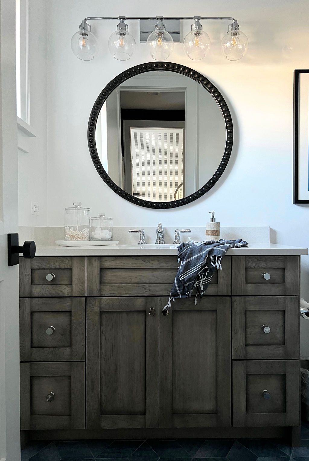 Bathroom vanity with gray cabinets, round mirror, and clear globe lights.
