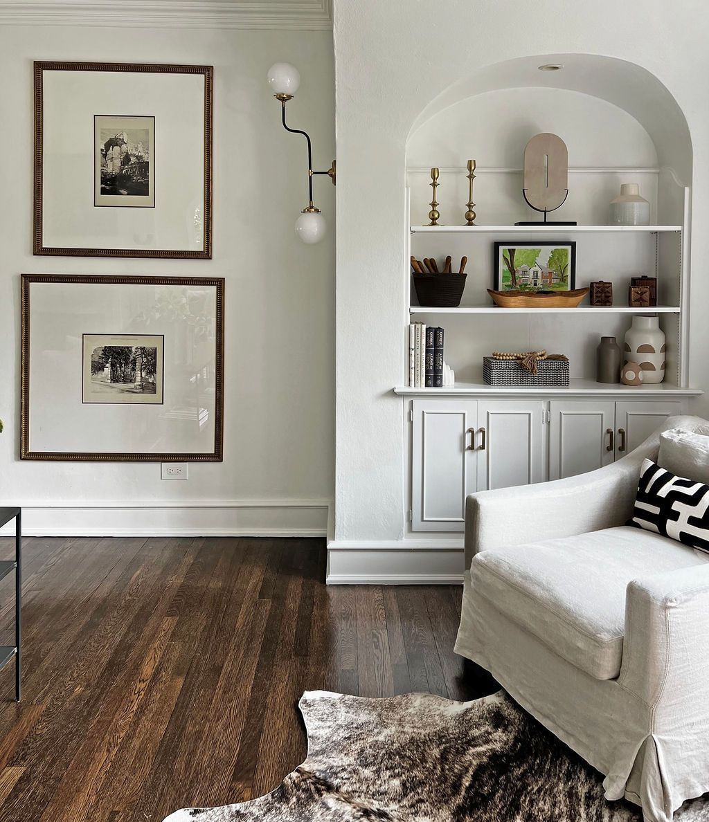 Cozy room with dark wood floor, built-in shelves, white armchair, framed artwork, and decorative fur rug.