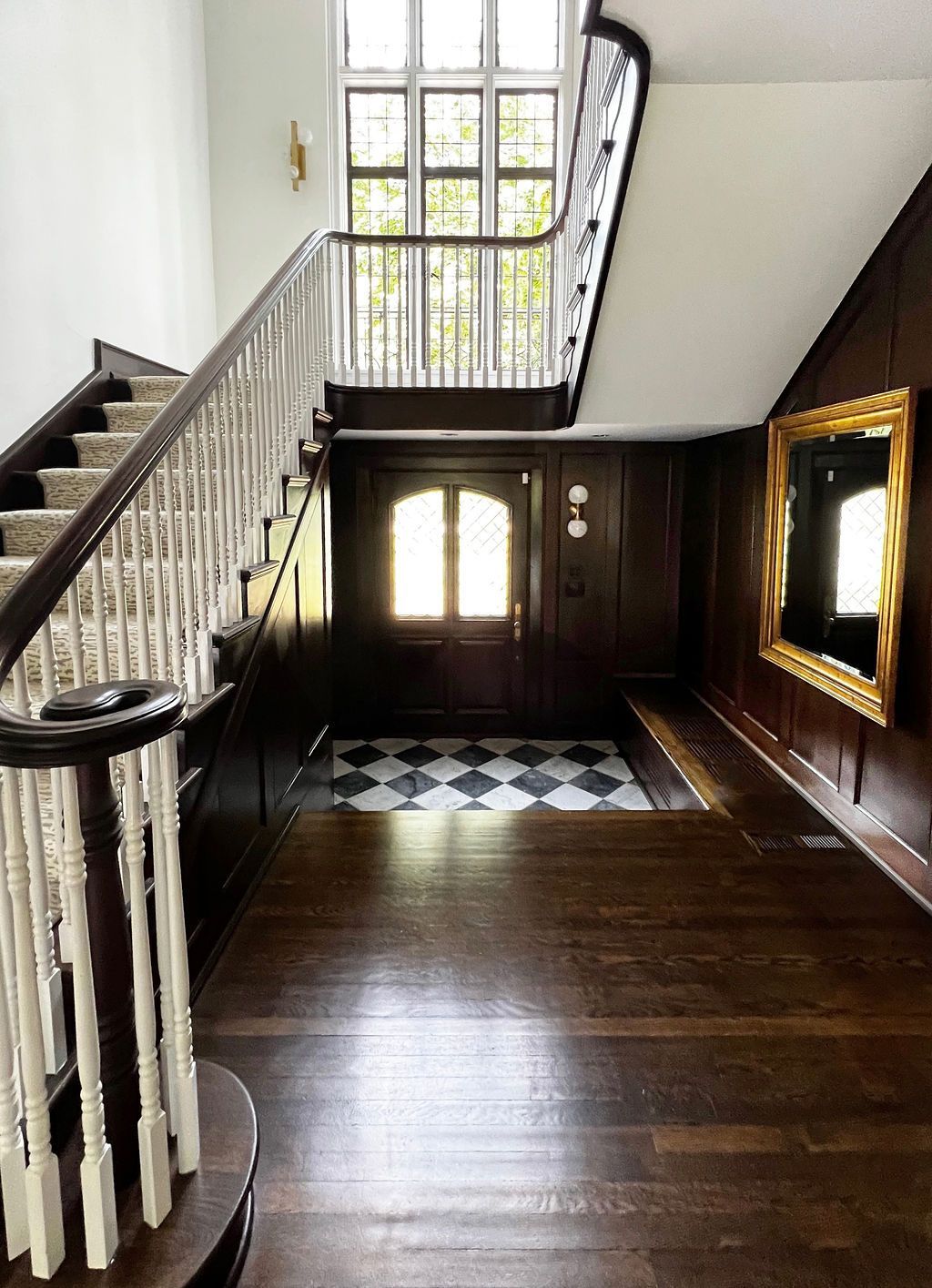 Grand entrance hall with staircase, dark wood paneling, checkered floor, and ornate doorway.