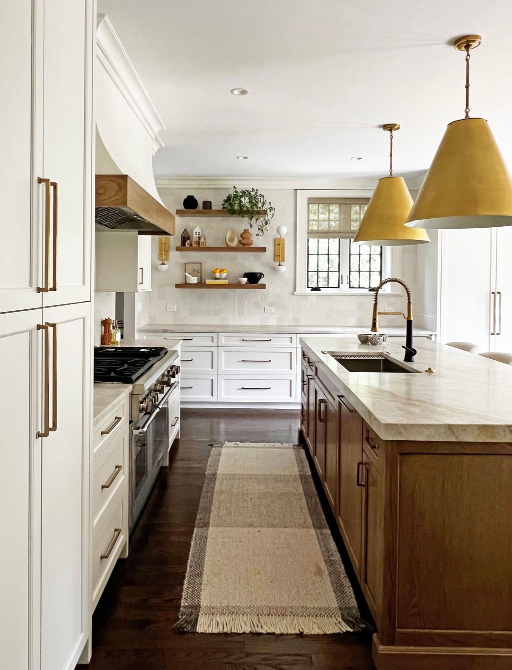 Kitchen with white cabinets, wood island, gold pendant lights, and runner rug.