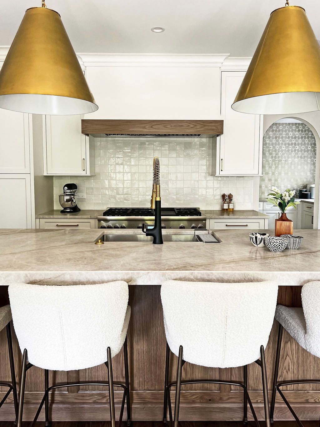 Kitchen with gold pendant lights, white cabinets, and bar stools with a brown and white color scheme.