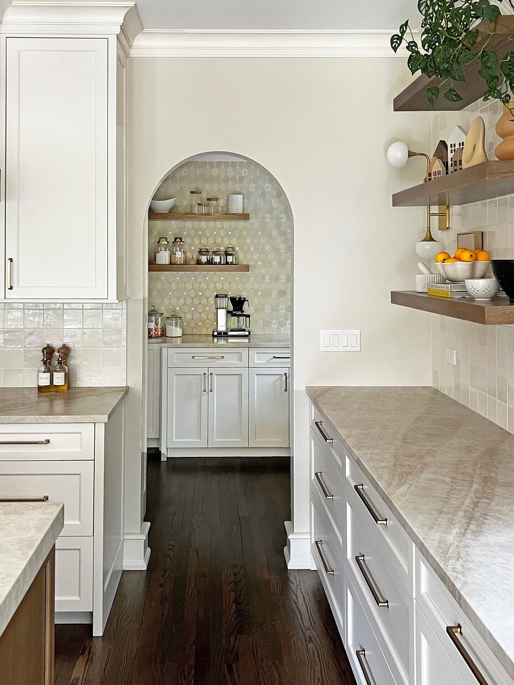 Kitchen with white cabinets, arched doorway, wooden shelves, and dark wood floor.
