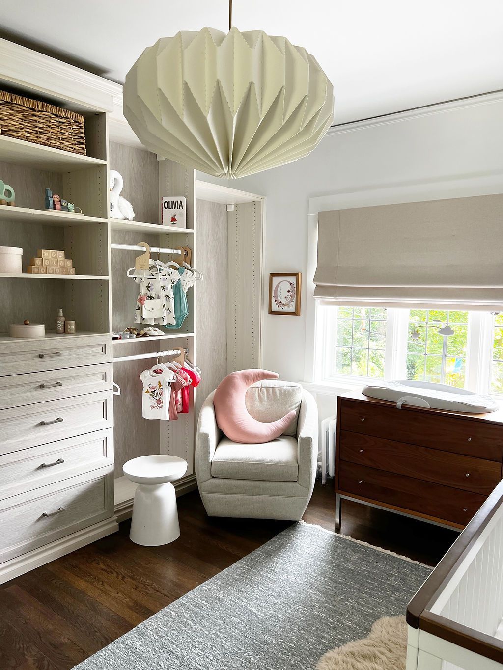 Baby nursery with neutral tones: closet, crib, chair, and changing table.  Light fixtures and rugs complete the space.