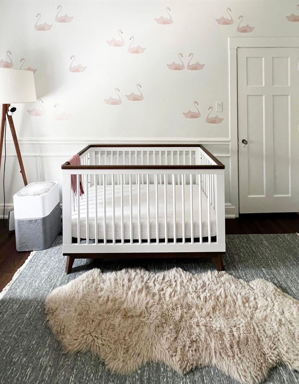 Nursery with white crib, flamingo wallpaper, plush rug, and neutral color scheme.