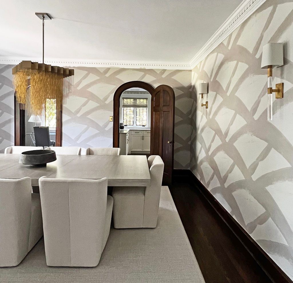 Dining room with patterned wallpaper, rectangular table, cream chairs, chandelier, and arched doorway.
