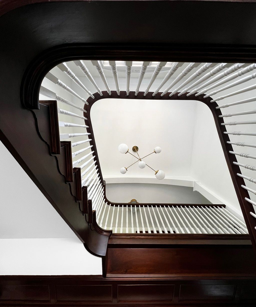 Dark wood staircase with white balusters, leading up to a landing with a chandelier.
