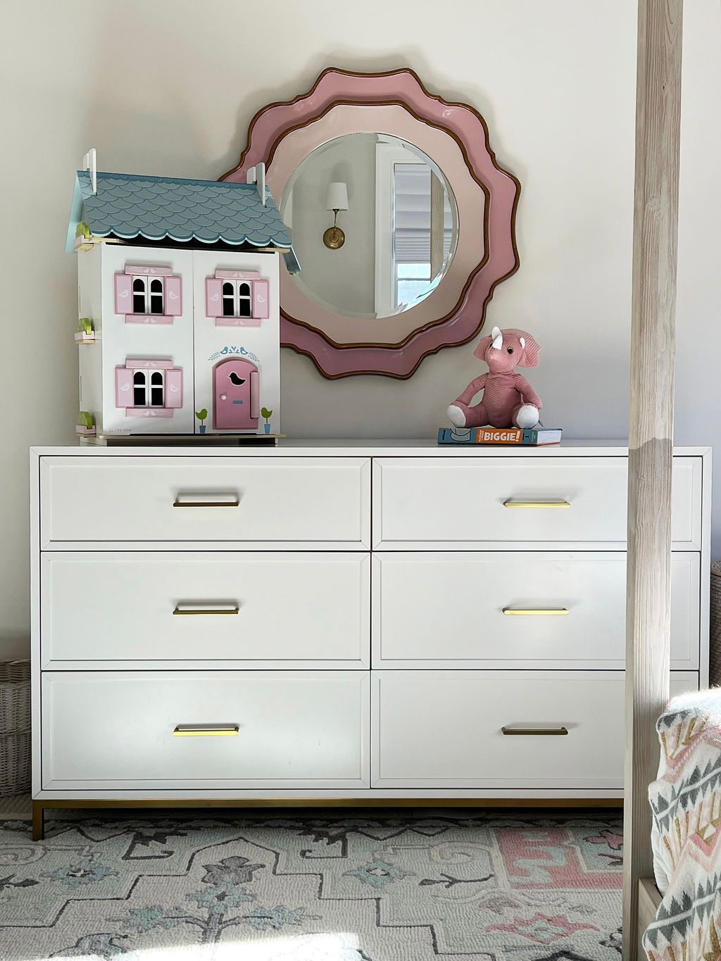 White dresser with dollhouse, pink mirror, toy, and rug.