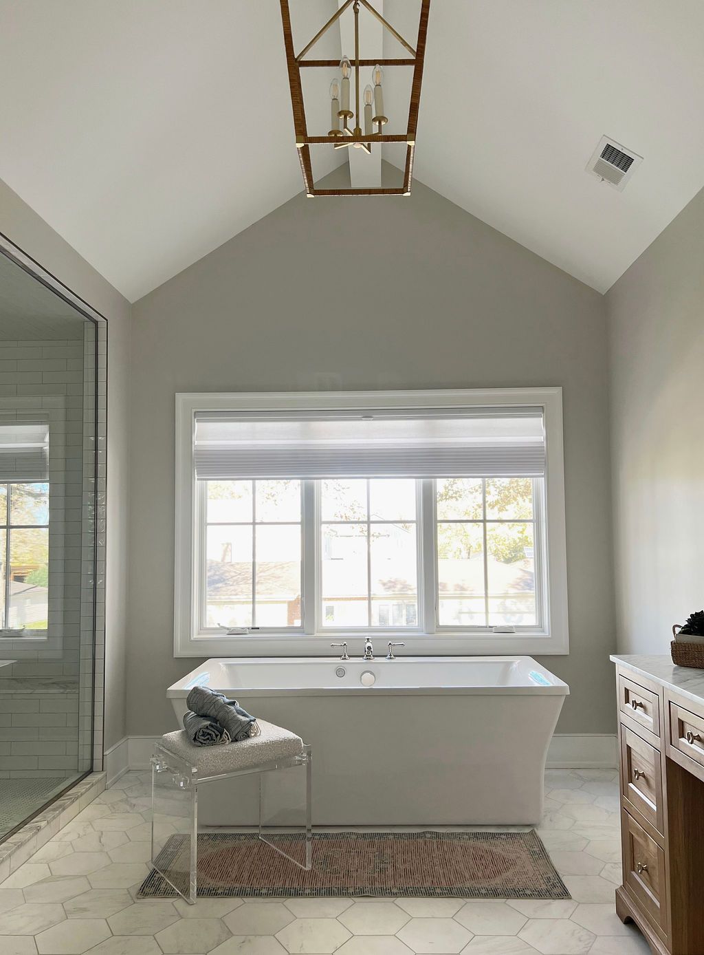 Bathroom with white bathtub under a window. Gray walls, white trim, and a gold light fixture.