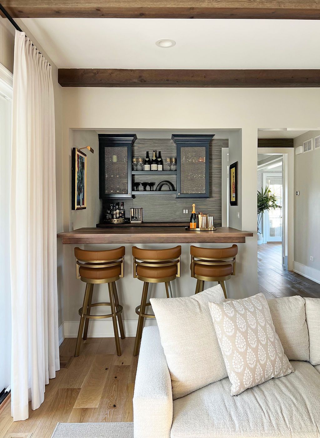 Cozy home bar with wooden bar top, three stools, and built-in cabinetry, overlooking a living area.
