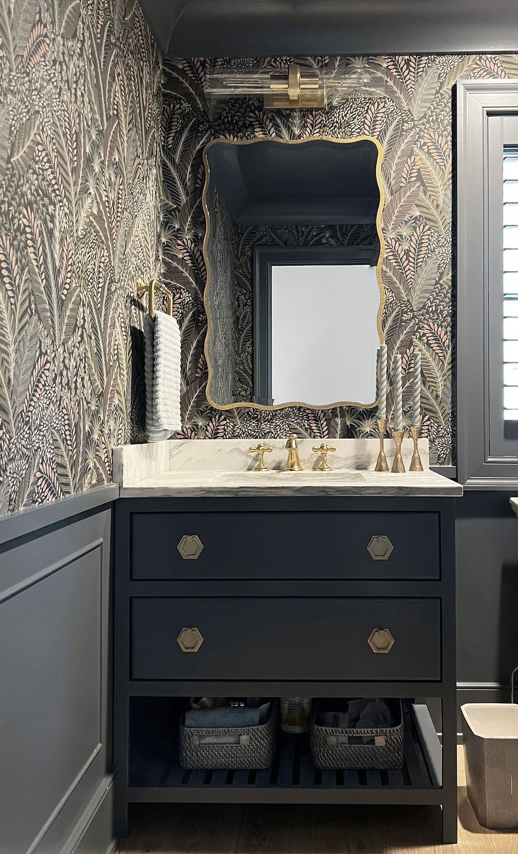 Dark blue vanity with gold hardware, marble countertop, and decorative mirror in bathroom with patterned wallpaper.
