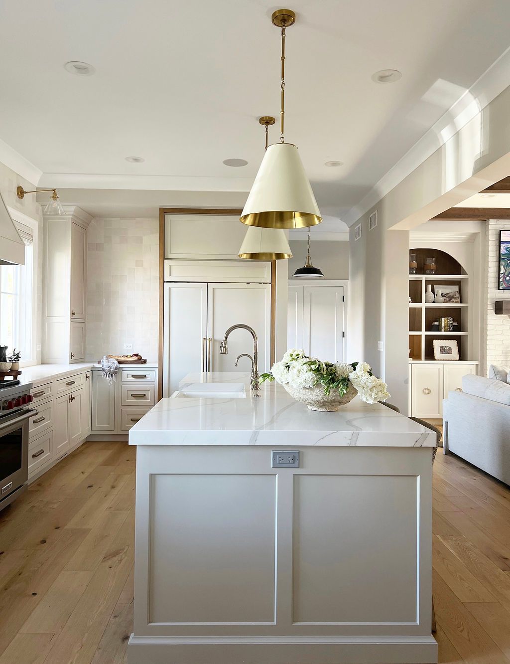 Elegant white kitchen with gray island, light wood floor, and pendant lights.