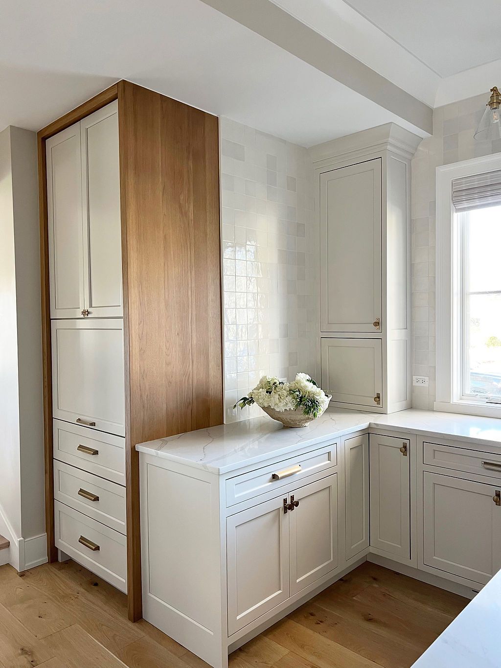 Kitchen corner with white cabinets, wooden accents, and a counter with floral arrangement.