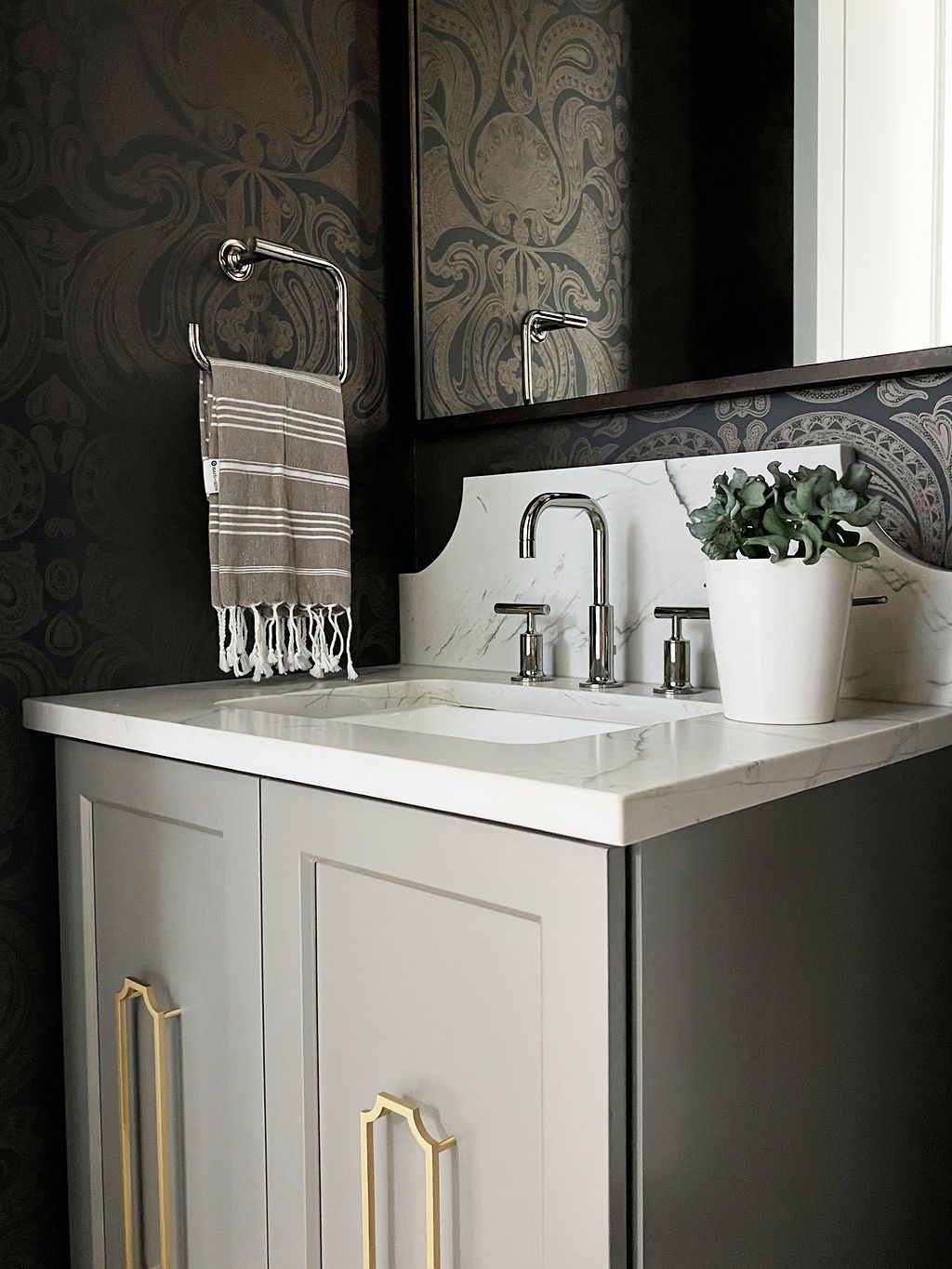 Bathroom vanity with gray cabinets, white countertop, silver faucet, and decorative patterned wallpaper.