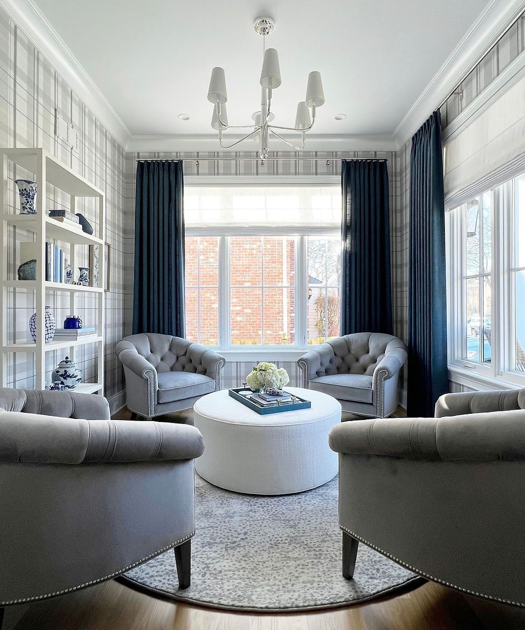 Living room with gray velvet chairs arranged around a white ottoman; blue drapes, and a chandelier.