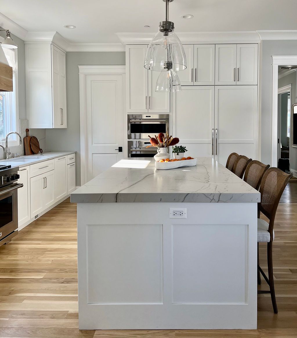 White kitchen with marble island, stainless steel appliances, and wood flooring.