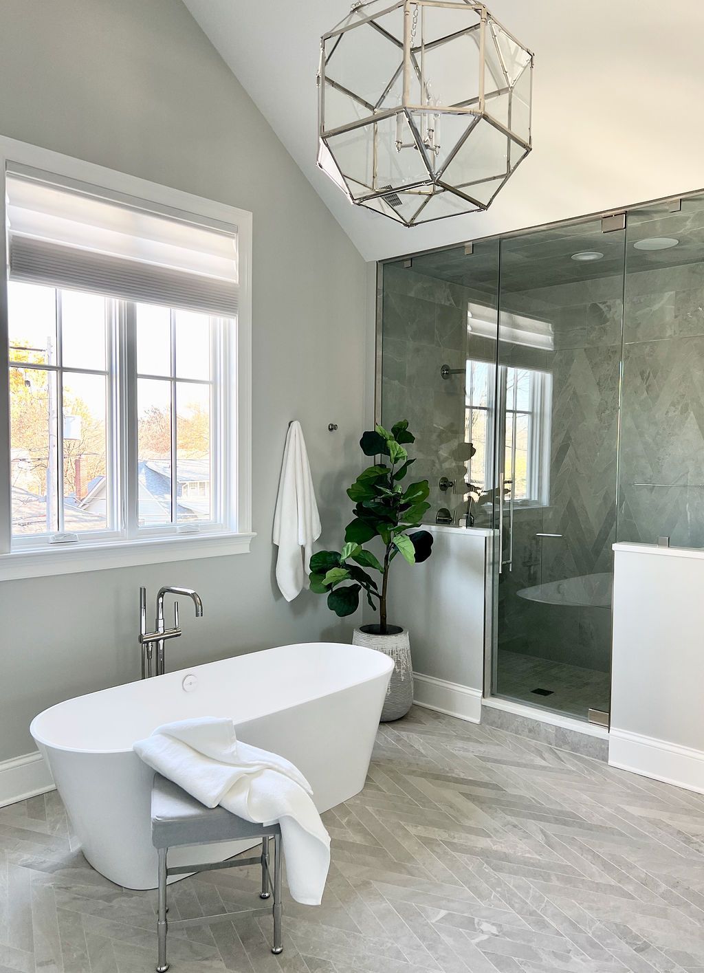 Modern bathroom with freestanding tub, glass shower, and geometric light fixture.