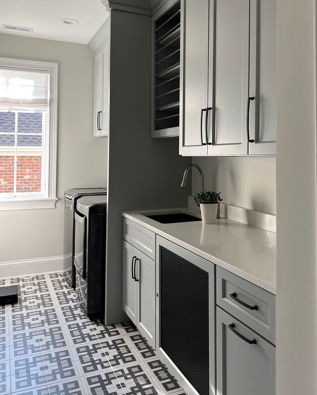 Laundry room with gray cabinets, sink, patterned floor, and a window.
