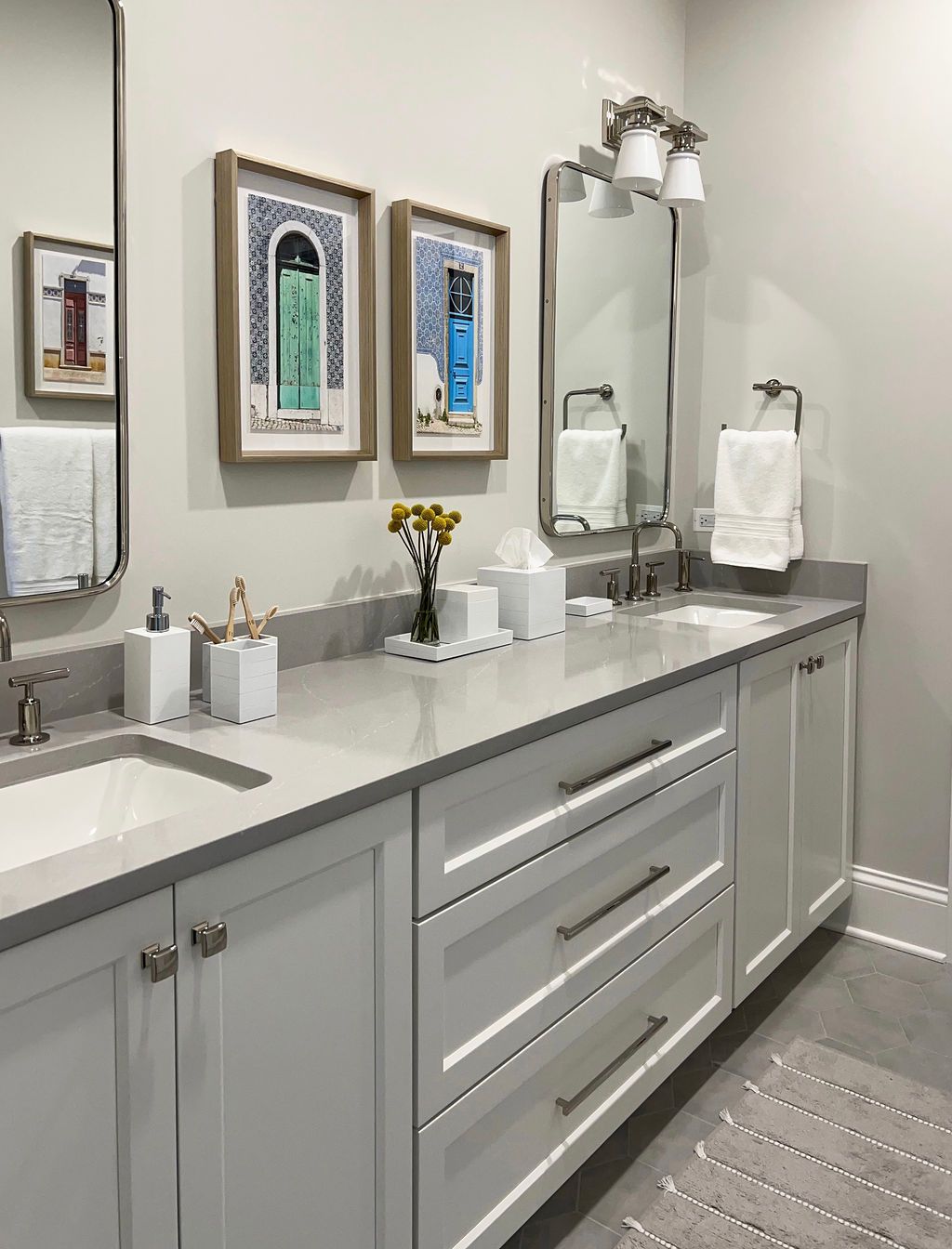 Modern bathroom with double sinks, white cabinets, artwork, and gray countertops.