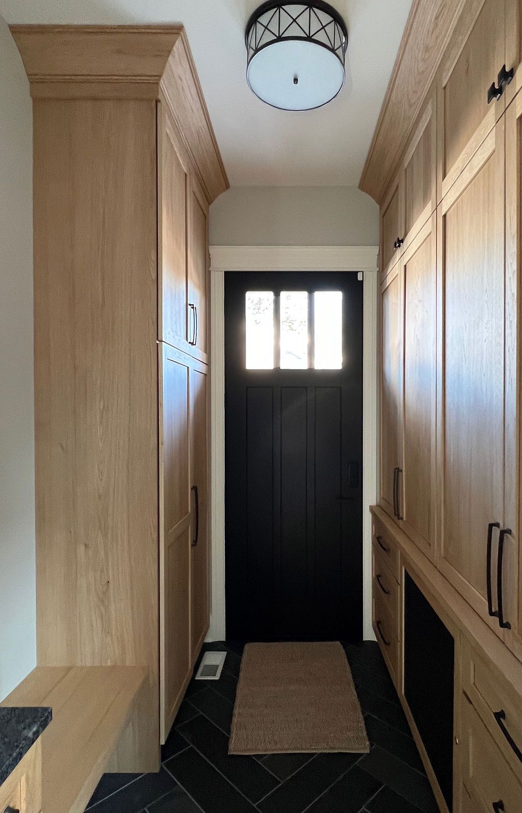 Entryway with wood cabinets, black door, and dark herringbone floor.