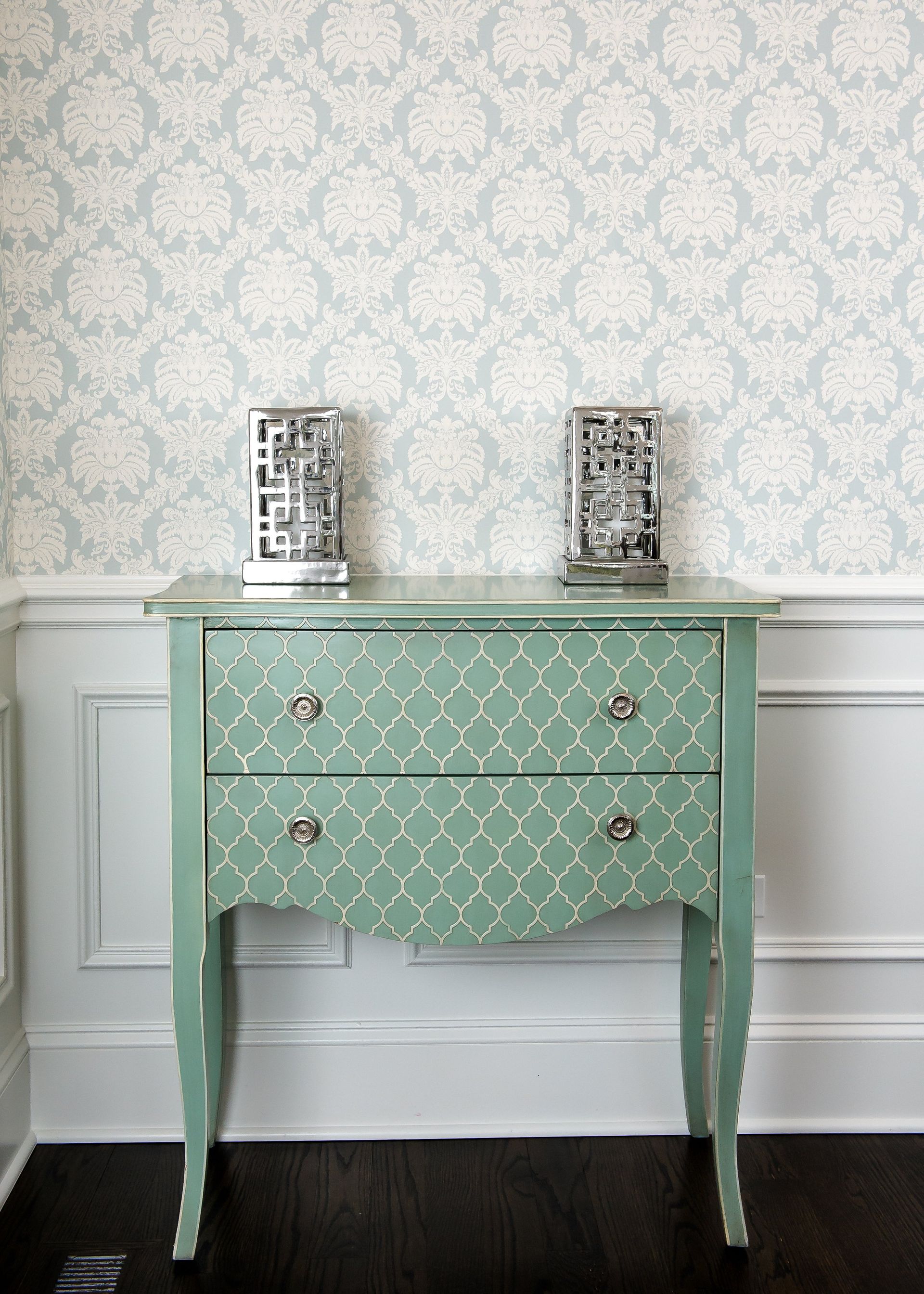 A green dresser with two lamps on top of it