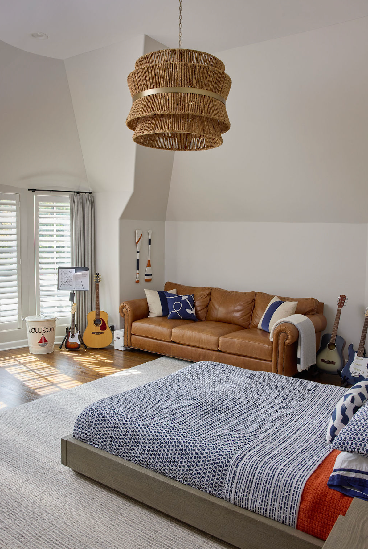 Bedroom with bed, leather sofa, guitars, and woven light fixture.