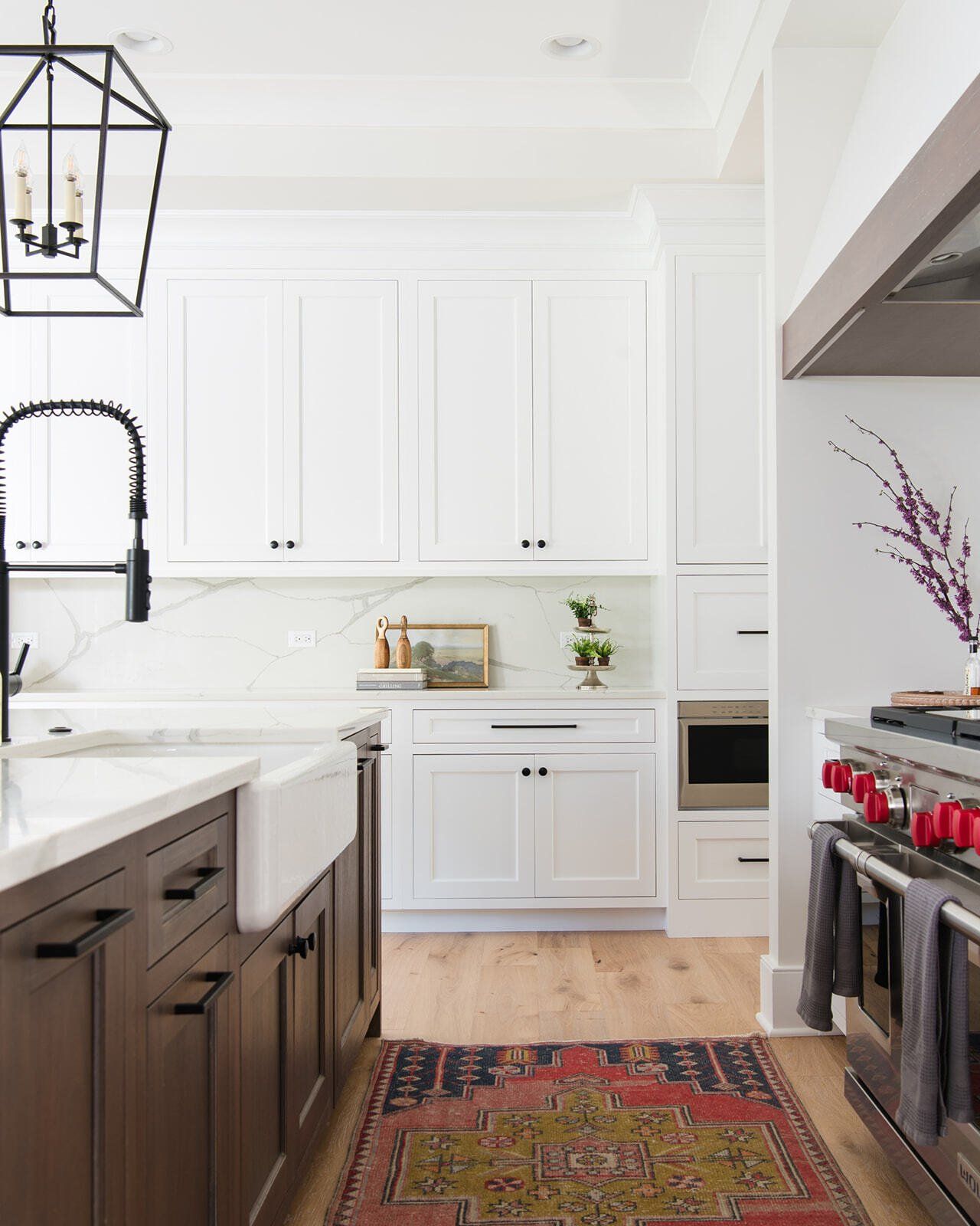 A kitchen with white cabinets , a stove , a sink , and a rug on the floor.