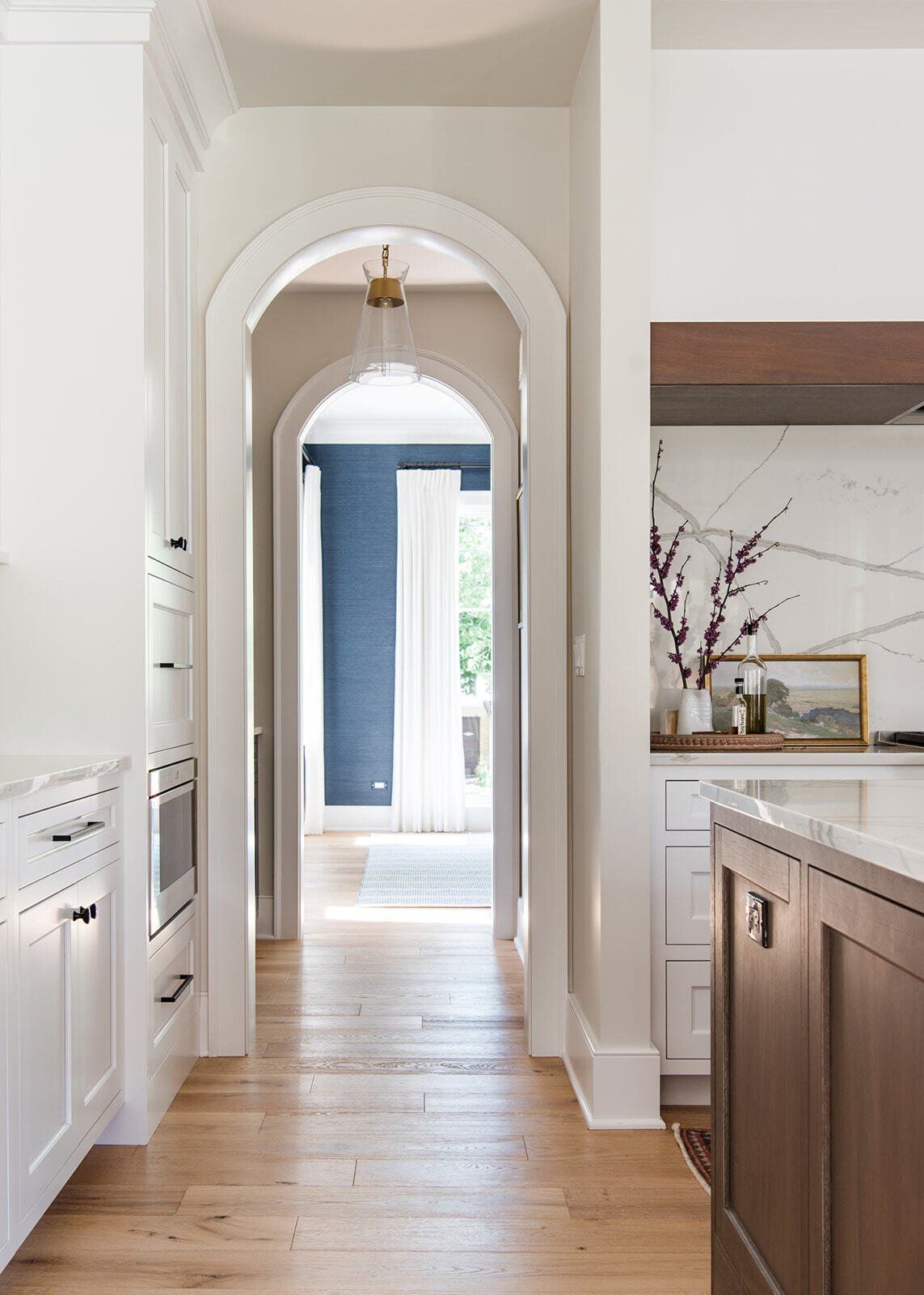 A kitchen with white cabinets and wooden floors leading to a hallway.