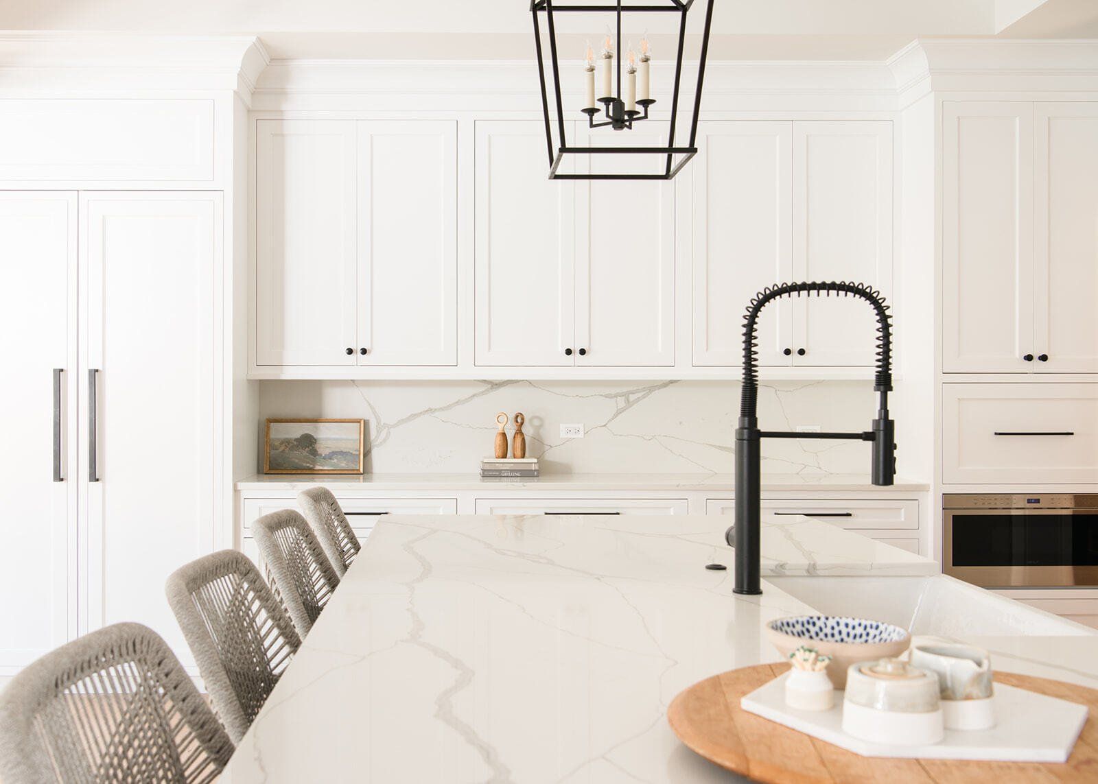 A kitchen with white cabinets , white counter tops , and a black faucet.