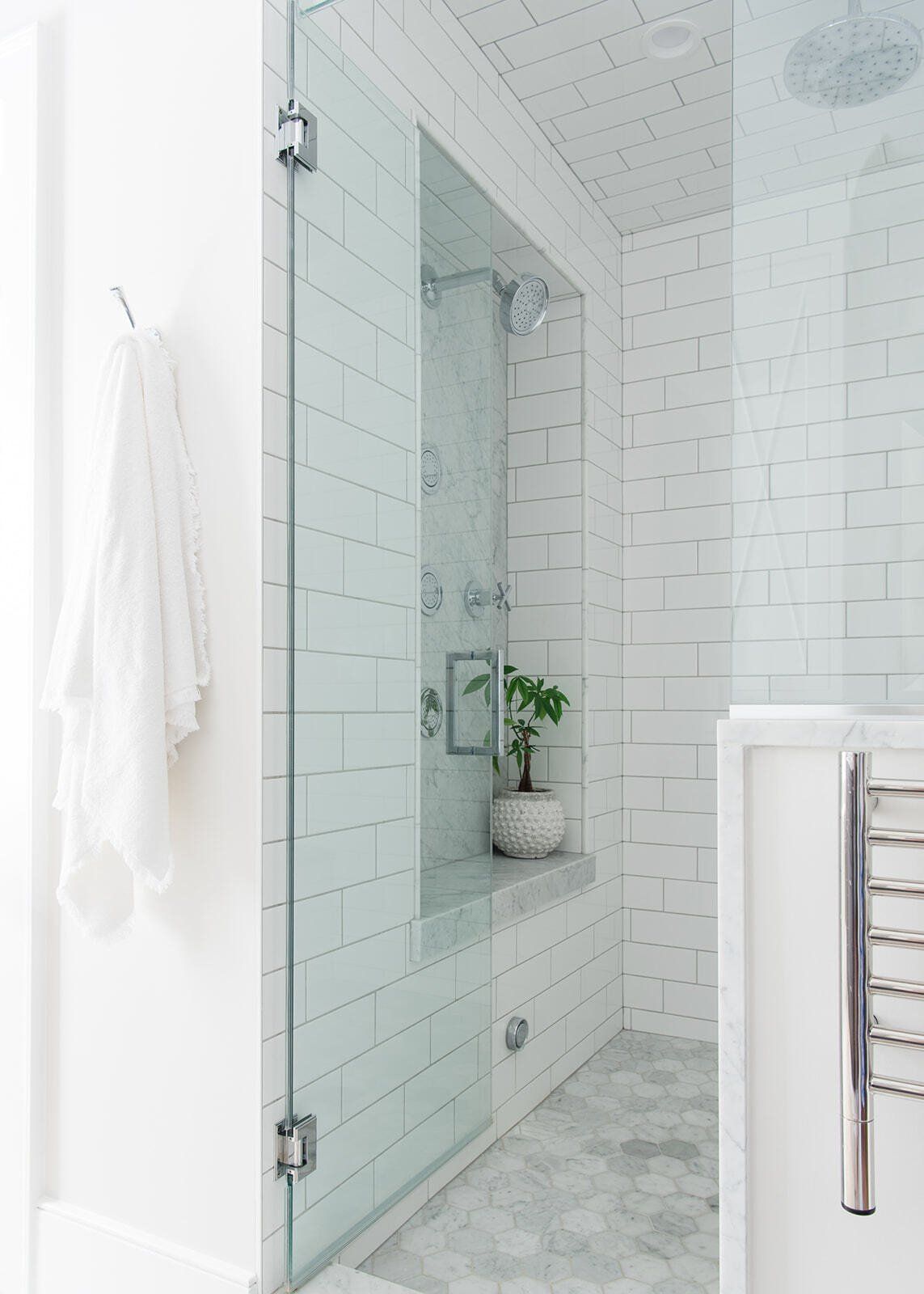 A bathroom with white tiles and a walk in shower with a glass door.