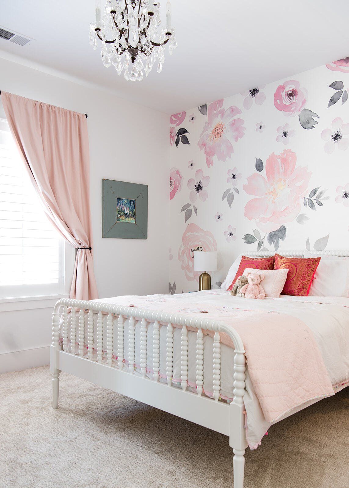 A bedroom with a white bed , pink curtains , and a chandelier.