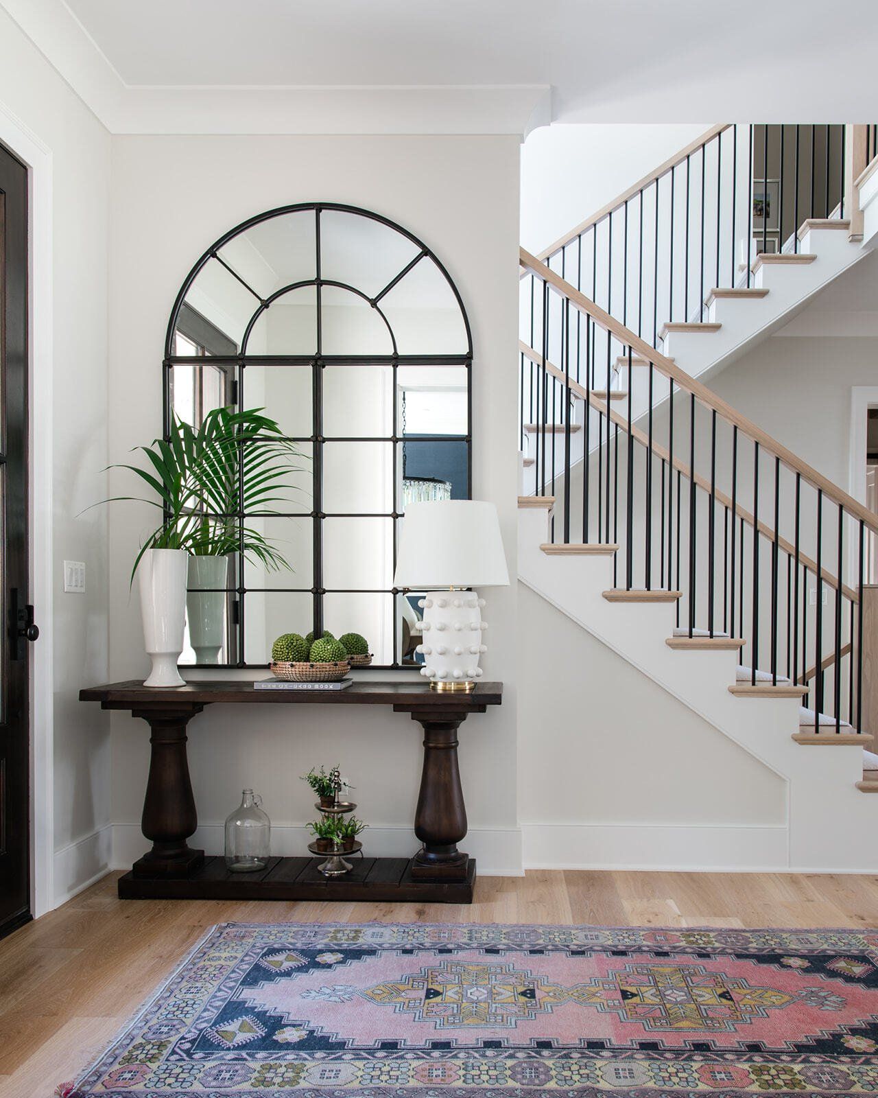 A hallway with a staircase , a table , a mirror and a rug.