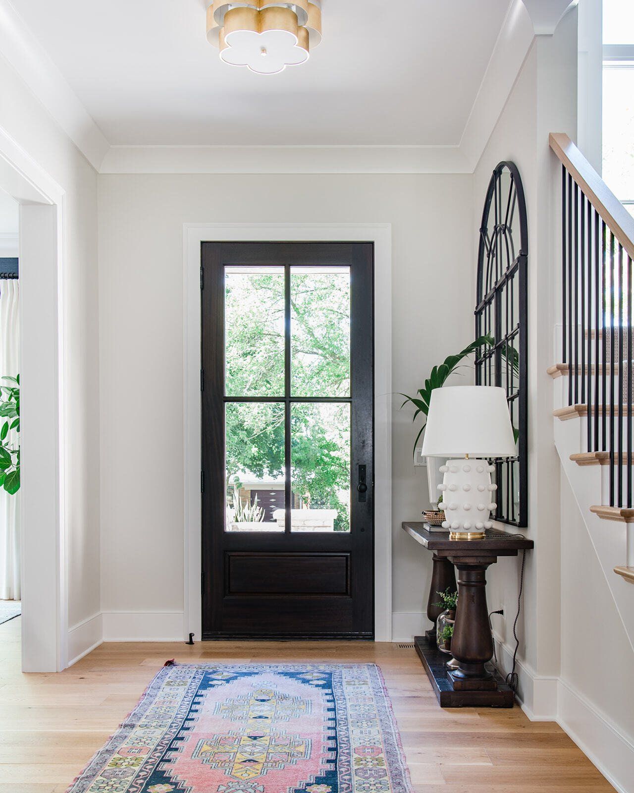 A hallway with a black door , rug , lamp and stairs.