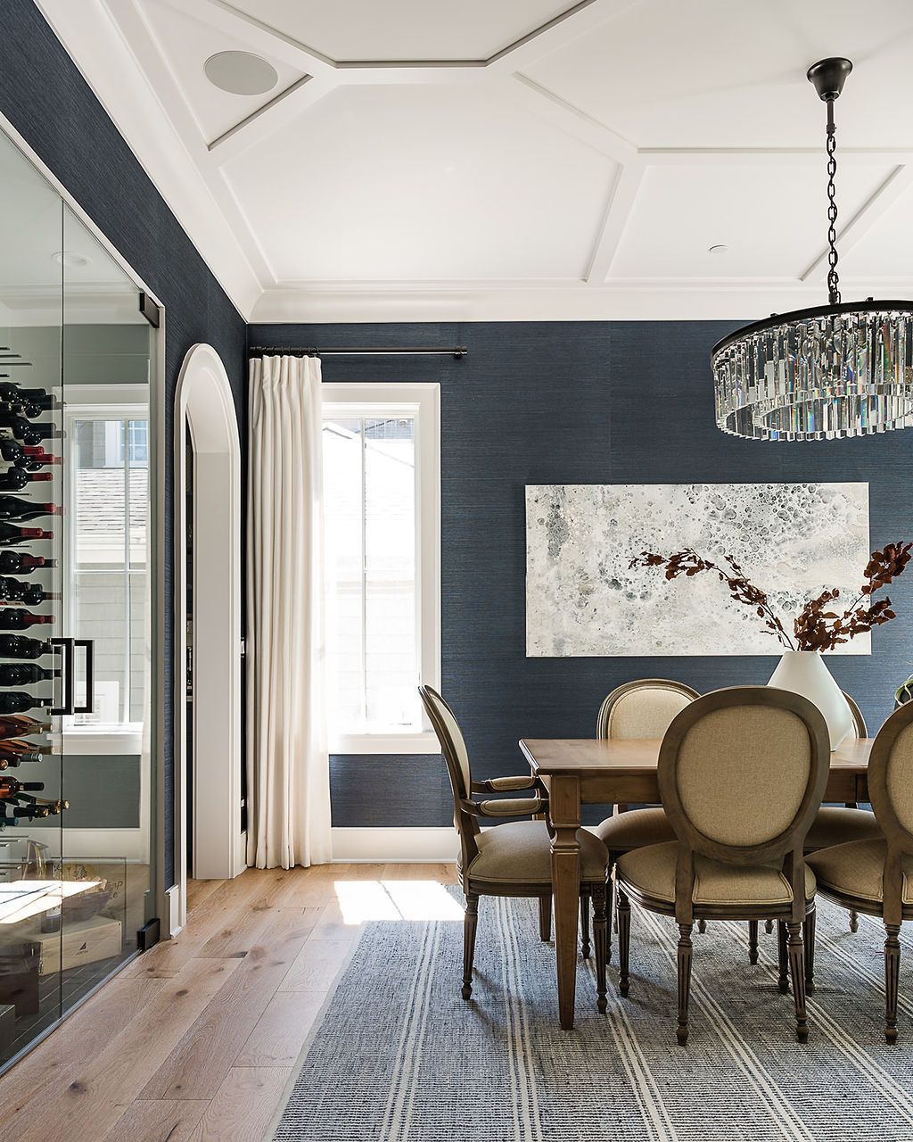 Elegant dining room with navy walls, crystal chandelier, wooden table and chairs, and a wine cellar.