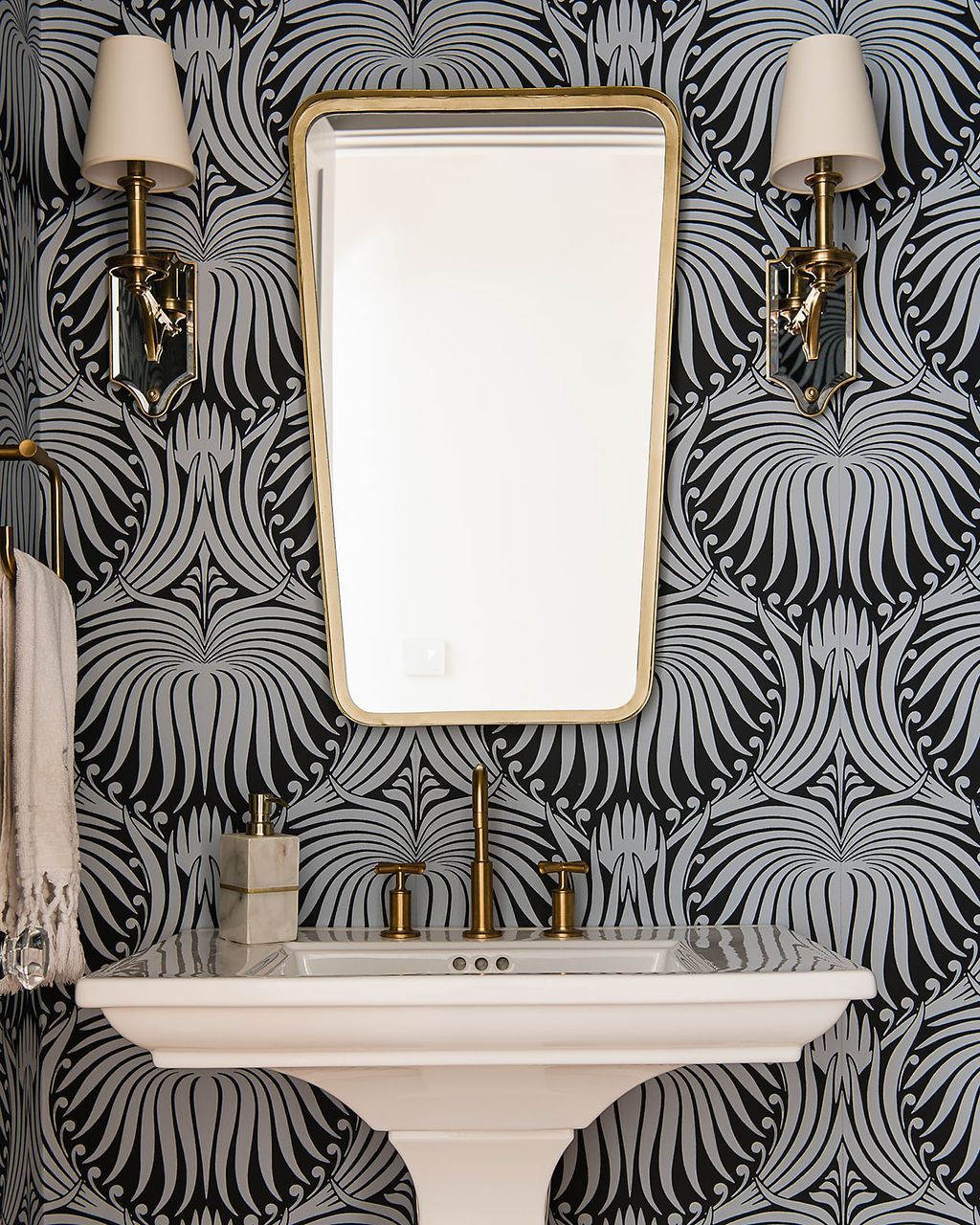 Bathroom with white pedestal sink, gold fixtures, and patterned blue and black wallpaper.