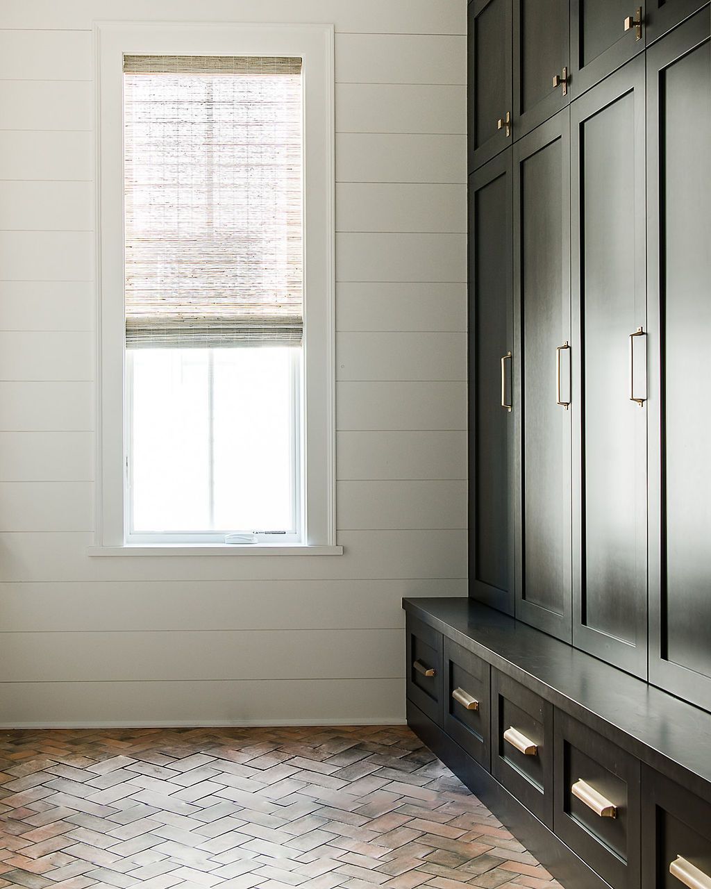 A room with a window and a built-in dark cabinet with drawers and bench.